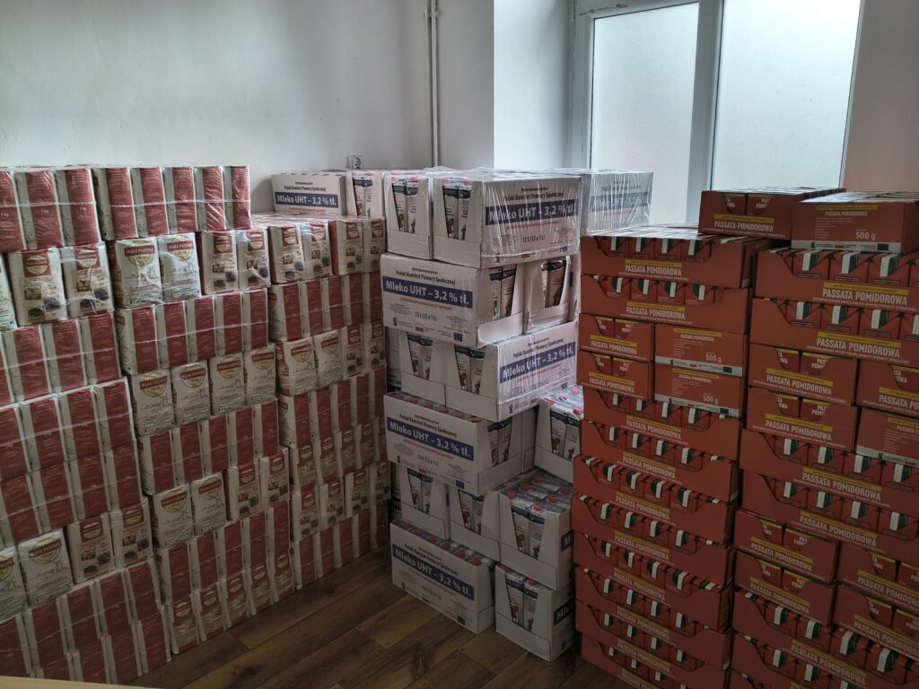 żywność poukładana w magazynie. Na zdjęciu znajdują się palety z mąką, mlekiem i passatą pomidorową